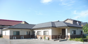 介護施設の建物外観。複数棟で構成された平屋建ての施設。駐車場が見える。