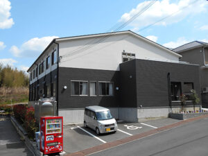 黒と白のツートンカラーの介護施設建物外観。駐車場と看板が見える