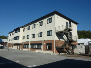 白色2階建ての介護施設の建物外観。駐車場から見た正面全景